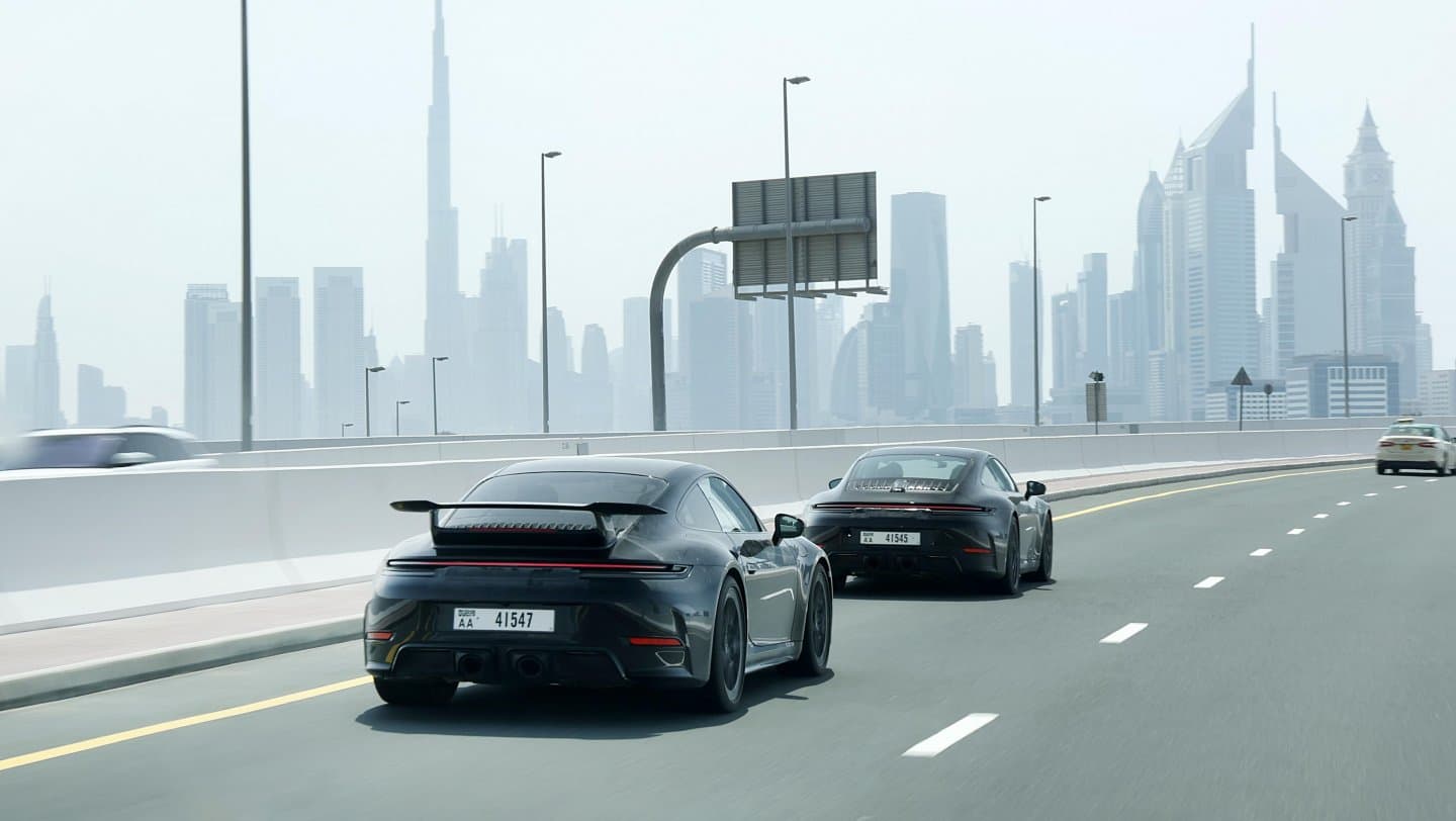 2025 Porsche 911 driving by large city skyline.